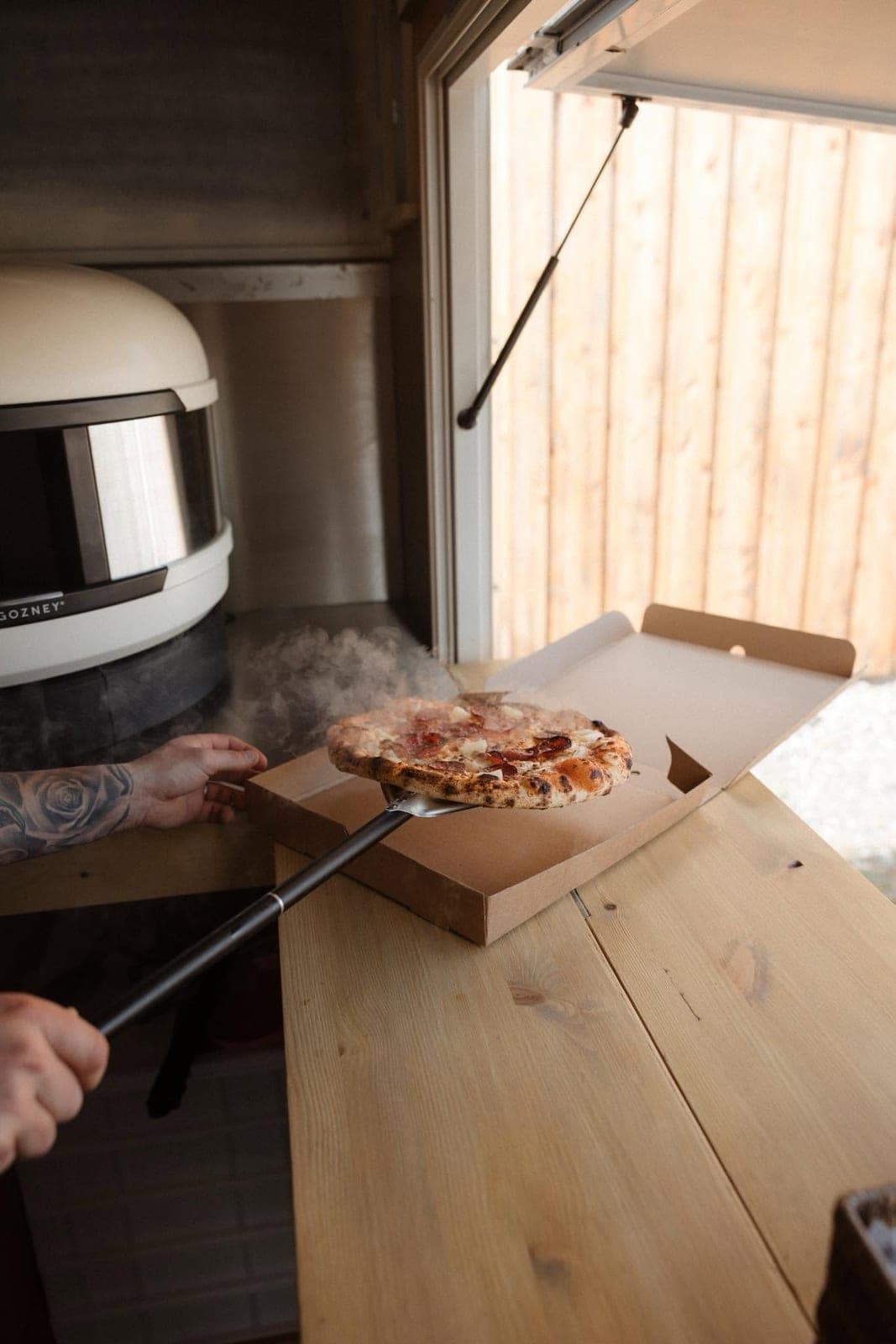 A sourdough pizza coming out of the Gozney oven inside the trailer, straight into a box