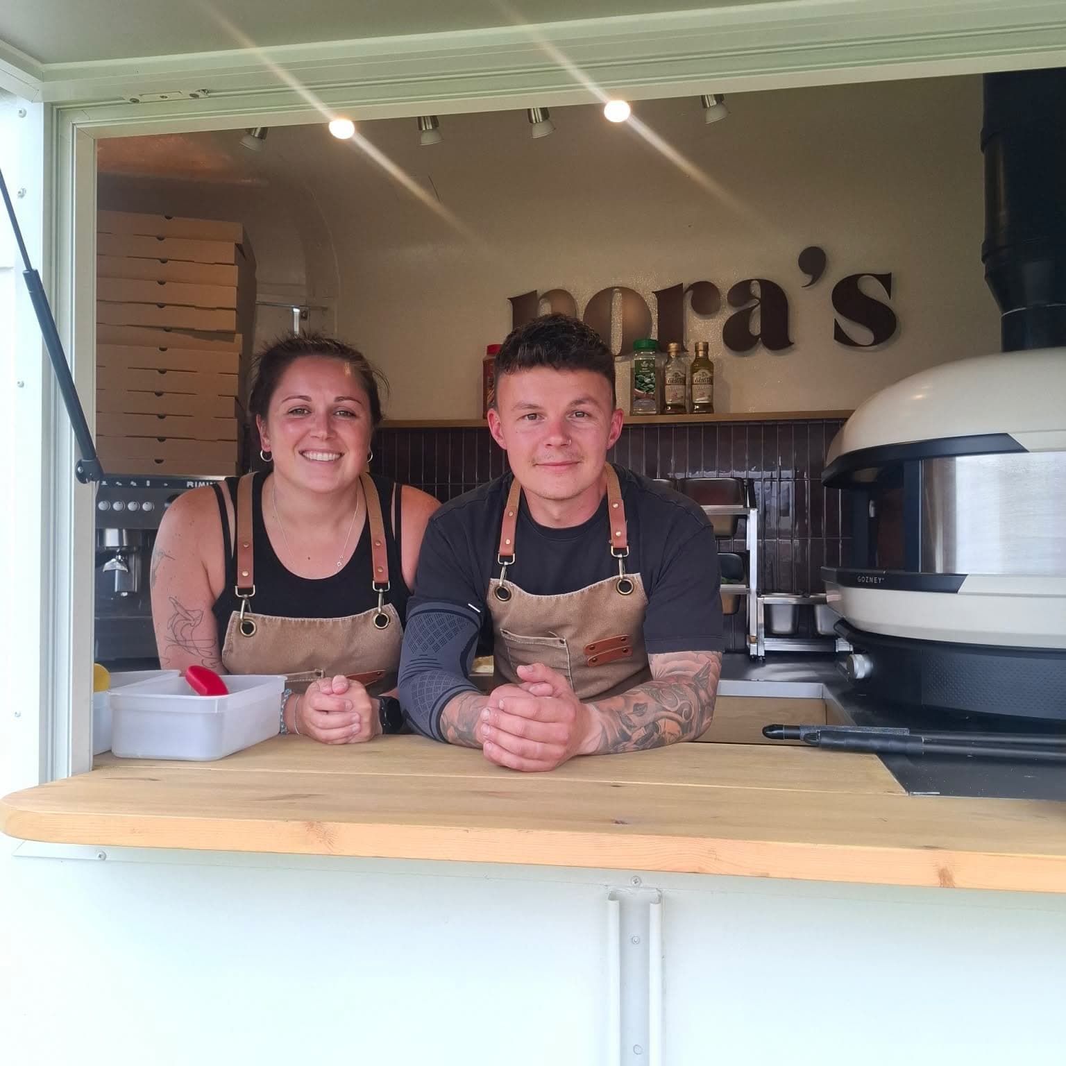 The Nora’s team smiling at the serving hatch, with the Gozney oven behind them